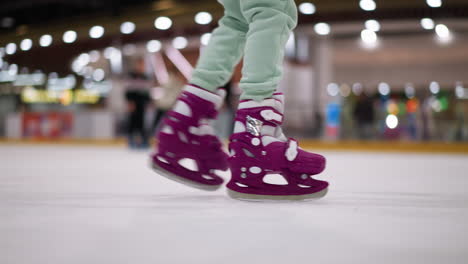 close-up of someone skating in purple ice skates on an ice rink, wearing ash-colored trousers, with other people skating in the background and a lively atmosphere