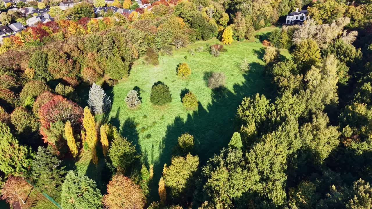 Drone shot of Parc de la Monniais in Cesson-Sévigné, Brittany, France, highlights open green lawns bordered by tall autumn trees and a business complex