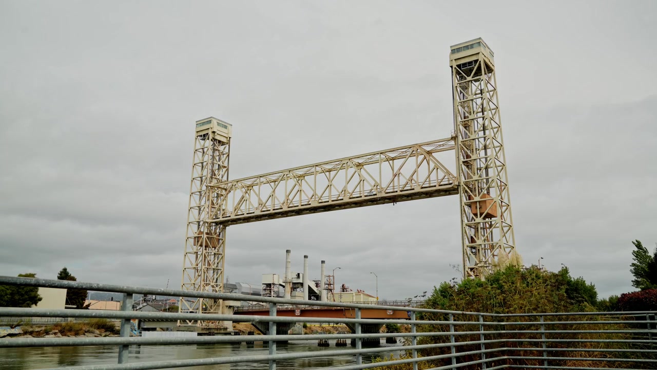 A vibrant time-lapse of the Fruitvale Bridge between Alameda and Oakland, California, highlights the traffic movement and boat activity below, framed by the shifting light of day and evening.