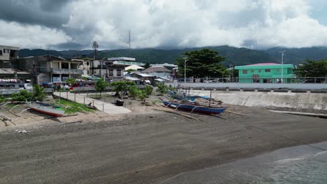 Approaching,-Establishing-drone-shot-of-island-town's-coastline-with-bangka-boats-and-jeepneys,-revealing-the-rural-community-of-Virac,-Catanduanes