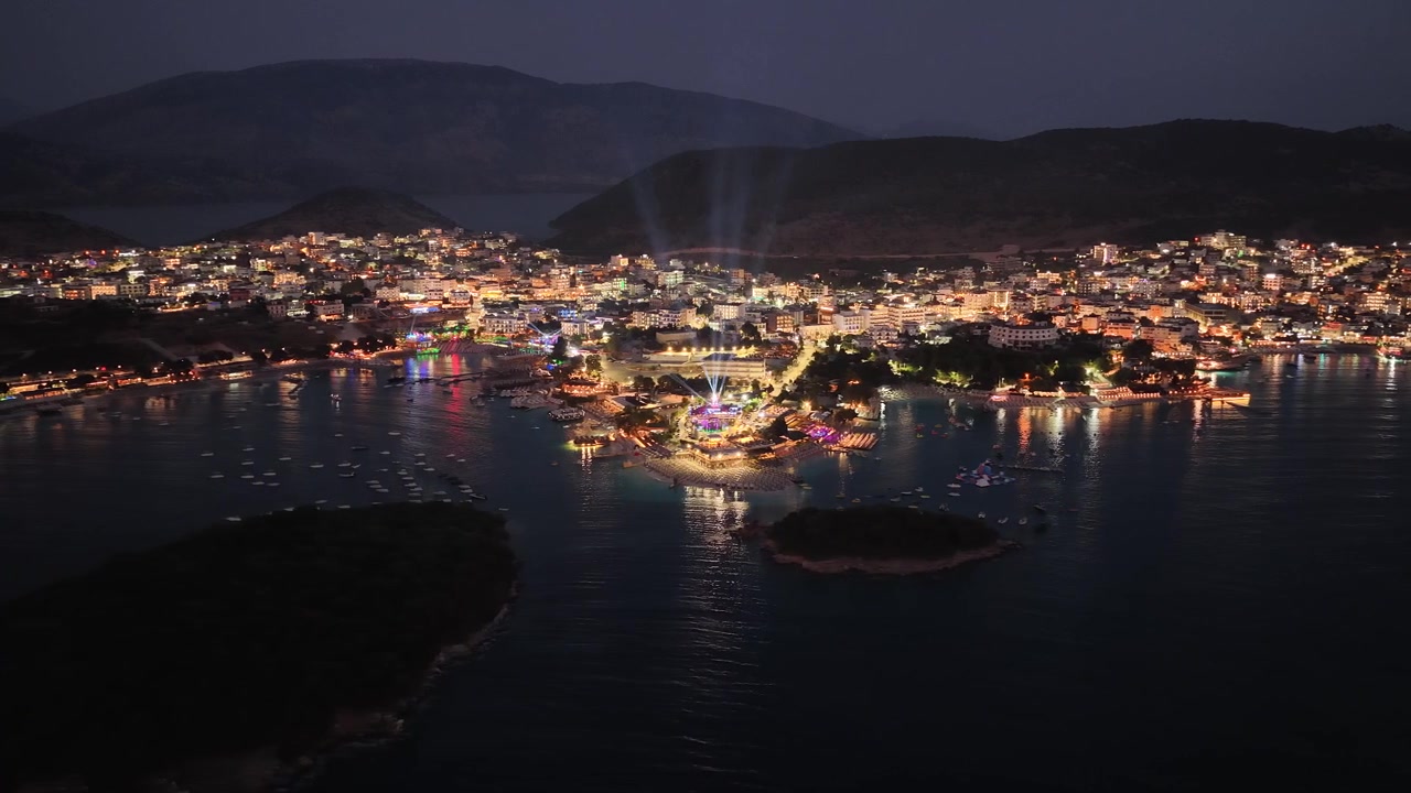 Cảnh đêm toàn cảnh rộng từ trên không của thị trấn nghỉ dưỡng Ksamil ở Albania với ánh đèn thành phố rực rỡ từ drone