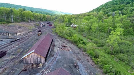 una vista aérea de una carretera ferroviaria de carbón de vía estrecha abandonada con tolvas oxidadas y vagones de carga y un edificio de apoyo que comienza a restaurarse