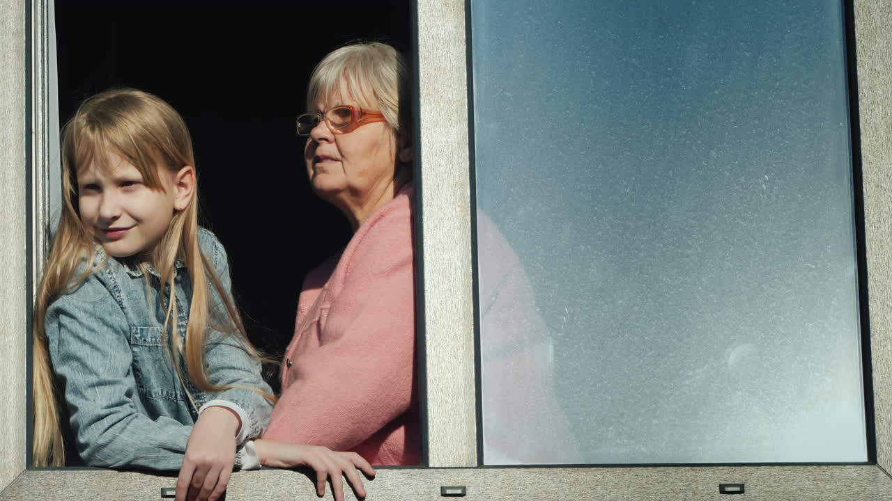 En ældre kvinde ved siden af barnet sidder i vindueskarmen og kigger ud af vinduet.