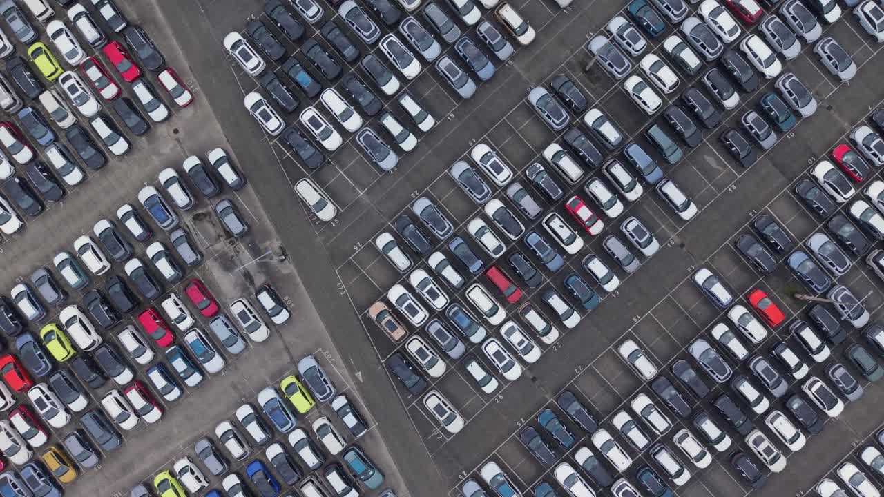 Ovenfra luftfoto af en stor parkeringsplads fyldt med parkerede biler arrangeret i pæne rækker. Videoen fremhæver bytransport, mobilitet og organiseret infrastruktur fra et droneperspektiv.