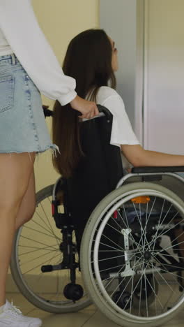 woman with friend in wheelchair stands near elevator waiting for door to open. lady takes care of person with disability helping to get to apartment