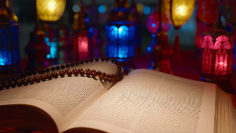 open holy book and prayer beads with illuminated islamic lanterns