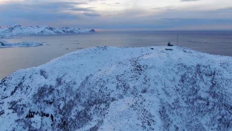 drone view in tromso area in winter flying over a snowy mountain peak with the sea on the horizon in norway