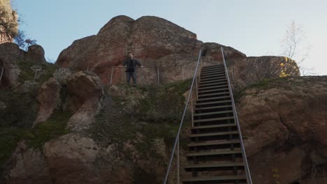 un disparo panorámico revela una escalera a lo largo de una ladera de la montaña, un hombre de pie contra un mirador, cielo azul y musgo creciendo en la formación rocosa de piedra arenisca