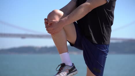 Cropped-shot-of-sportsman-stretching-leg-at-riverside