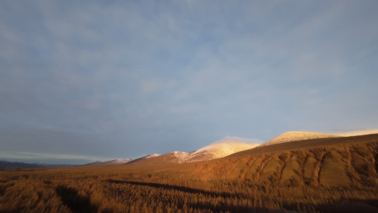 Explore the vast and majestic landscapes of Yakutia as a drone elegantly glides over the scenic terrain, showcasing the magnificent mountains and rich wilderness bathed in golden sunlight.