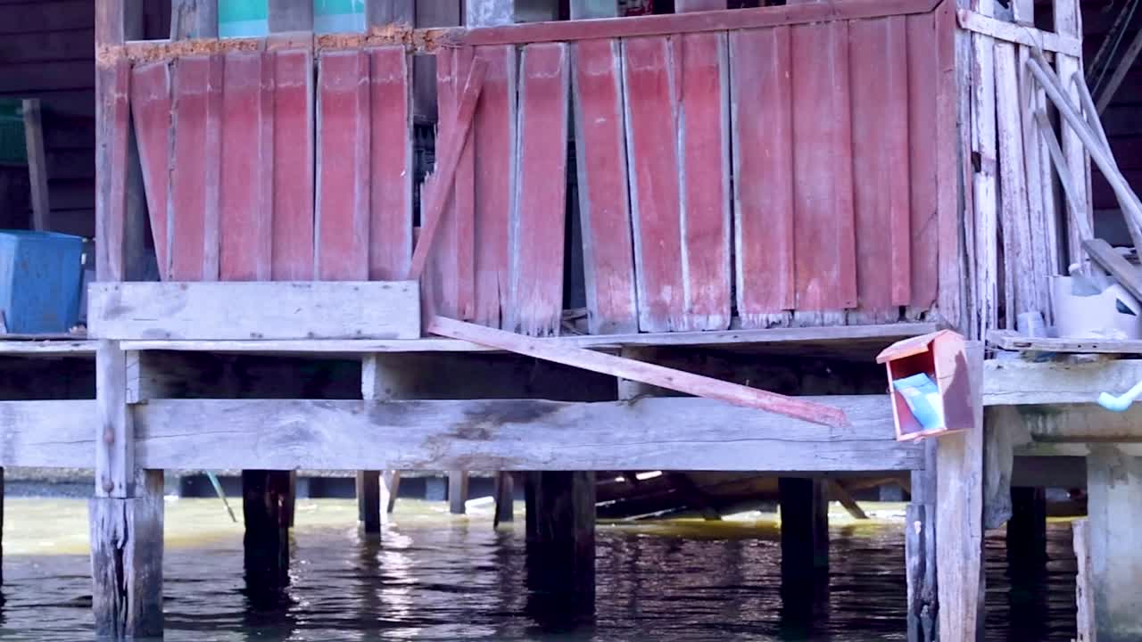 Detailed view of a weathered wooden platform by the water, featuring vines and scattered household items.