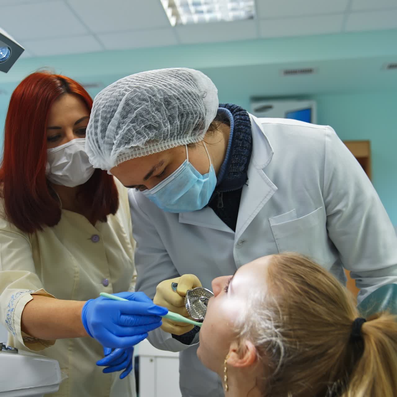 Estudiante de odontología inserta un instrumento metálico en la boca del paciente. El profesor guía y ayuda al estudiante.