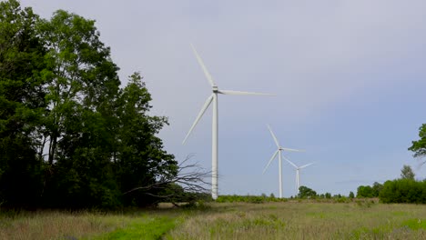 Las-Imágenes-Muestran-Turbinas-Eólicas-Eléctricas-De-Energía-Renovable-En-Estonia,-Harjumaa,-Europa,-Que-Giran-En-Cámara-Lenta-Durante-El-Verano-Mientras-El-Sol-Brilla-Y-La-Naturaleza-Las-Rodea.