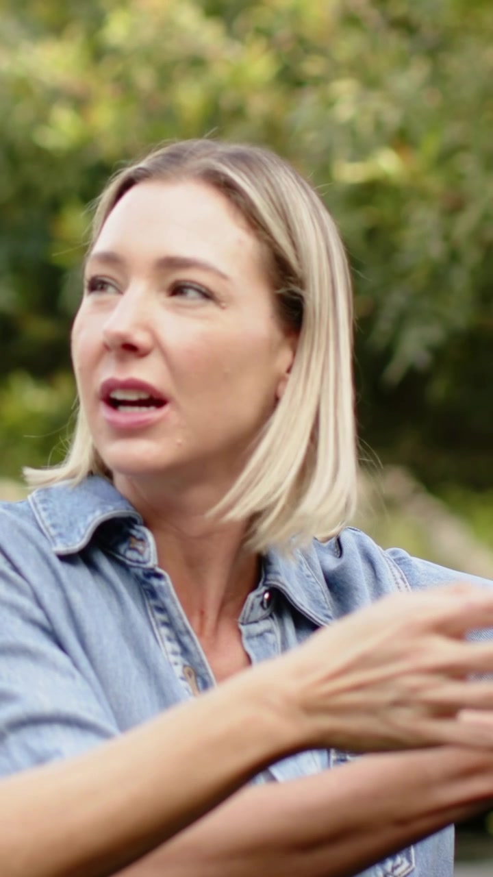 Vertical video: Saying woman leaning, gesturing in garden, explaining to friend, denim shirt, hoops