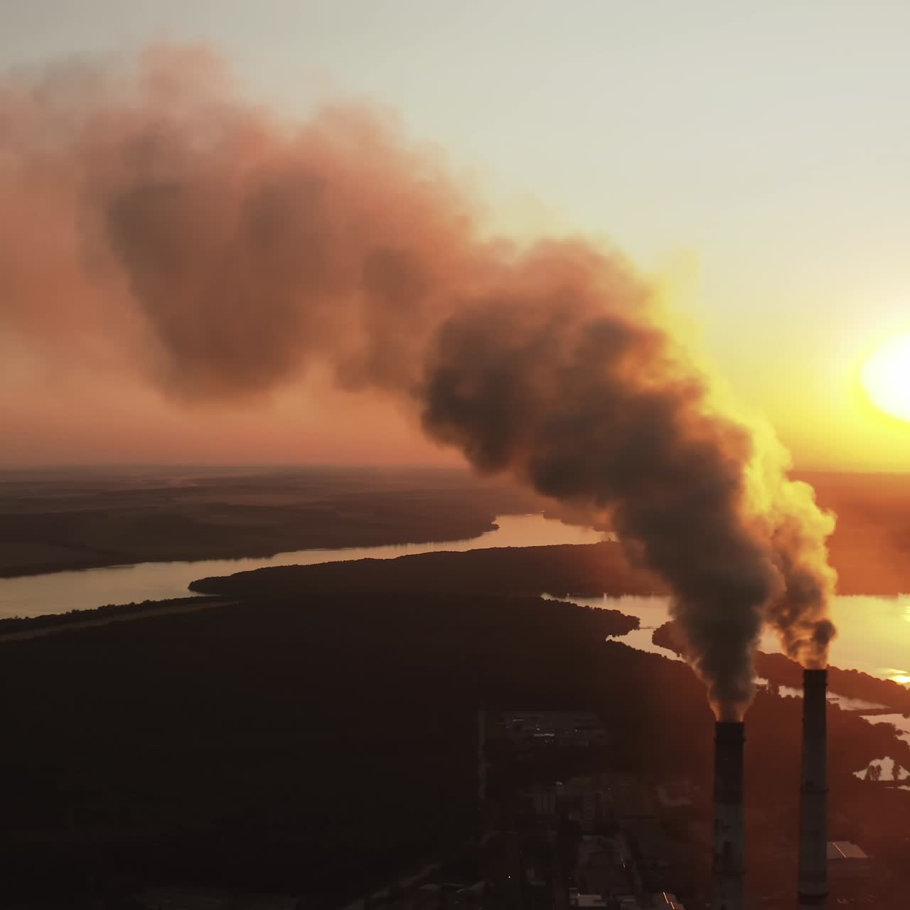 Large plant with smoking pipes. Dark smoke comes out in clouds from chimney of factory plant