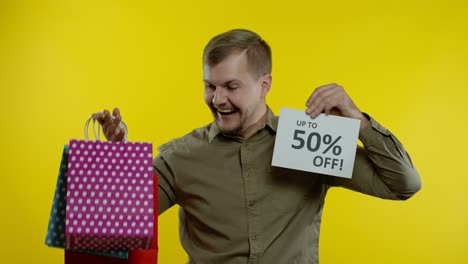 man showing shopping bags and up to 50 percent off inscription, looking satisfied with low prices