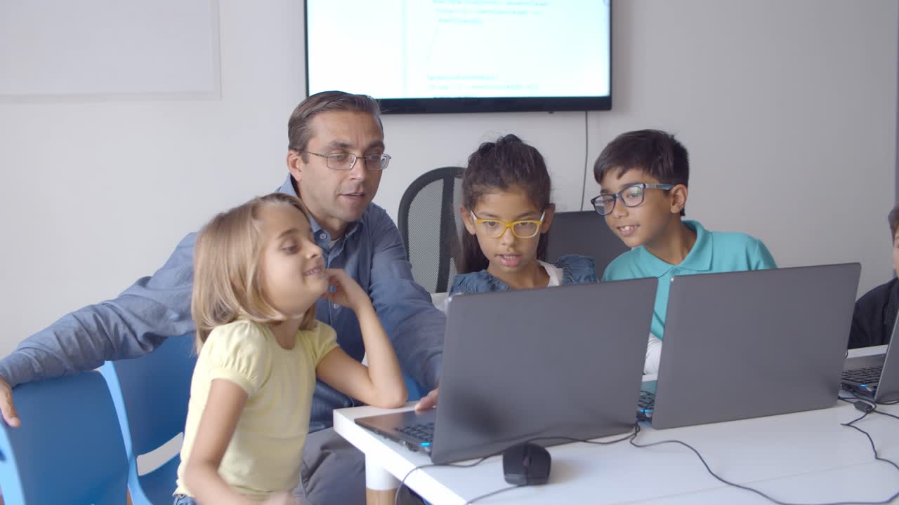 Computer science teacher sitting at desk near children