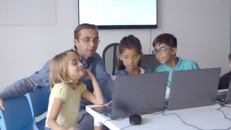 computer science teacher sitting at desk near children