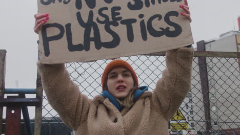 close up view of young female activist holding a cardboard placard and protesting to save the earth during a climate change protest while looking at camera