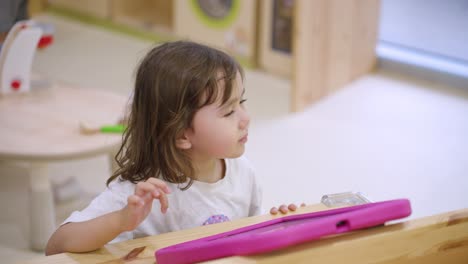 little girl creating art in an indoor playground, having fun and exploring creativity as she smiles and laughs at table, medium static, slow motion