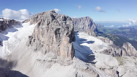 Aerial-panning-shot-showing-the-Sella-massif-in-the-Dolomites,-revealing-the-Sassolungo-range-in-the-background-on-a-sunny-day,-with-snow