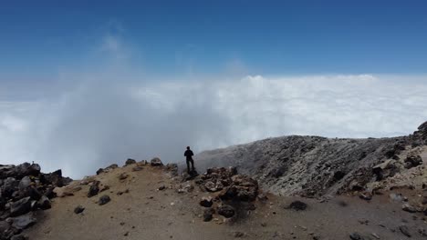 hombre de pie en el borde del cráter del volcán mirando el cielo de nubes por debajo