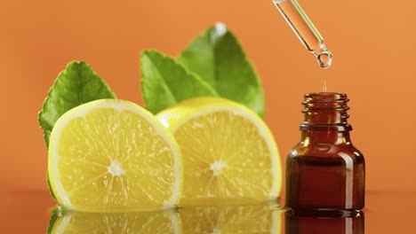 dripping lemon juice from pipette into bottle close-up, vitamin oil. making aroma serum on orange background. dropping liquid citrus extract, skincare routine, treatment spa. traditional medicine