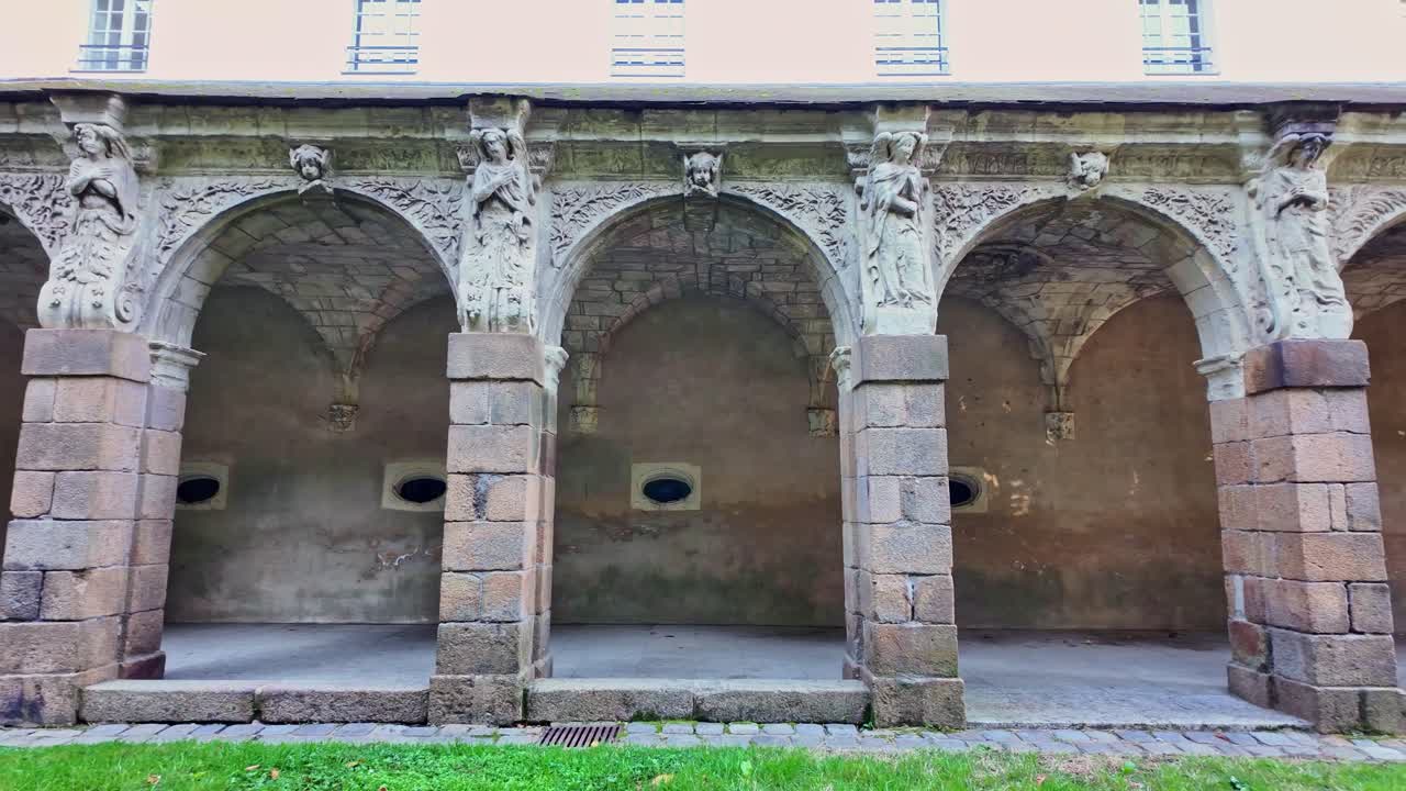 Ground shot showing stone arches, columns, and sculptures in the courtyard behind Notre-Dame en Saint-Melaine Church in Rennes, France