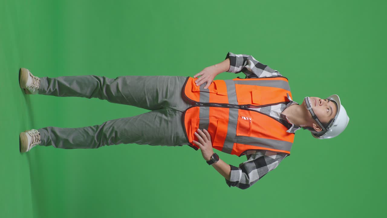 Full Body Of Asian Male Engineer Wearing Safety Helmet Looking Around While Standing With Arms Akimbo In The Green Screen Background Studio
