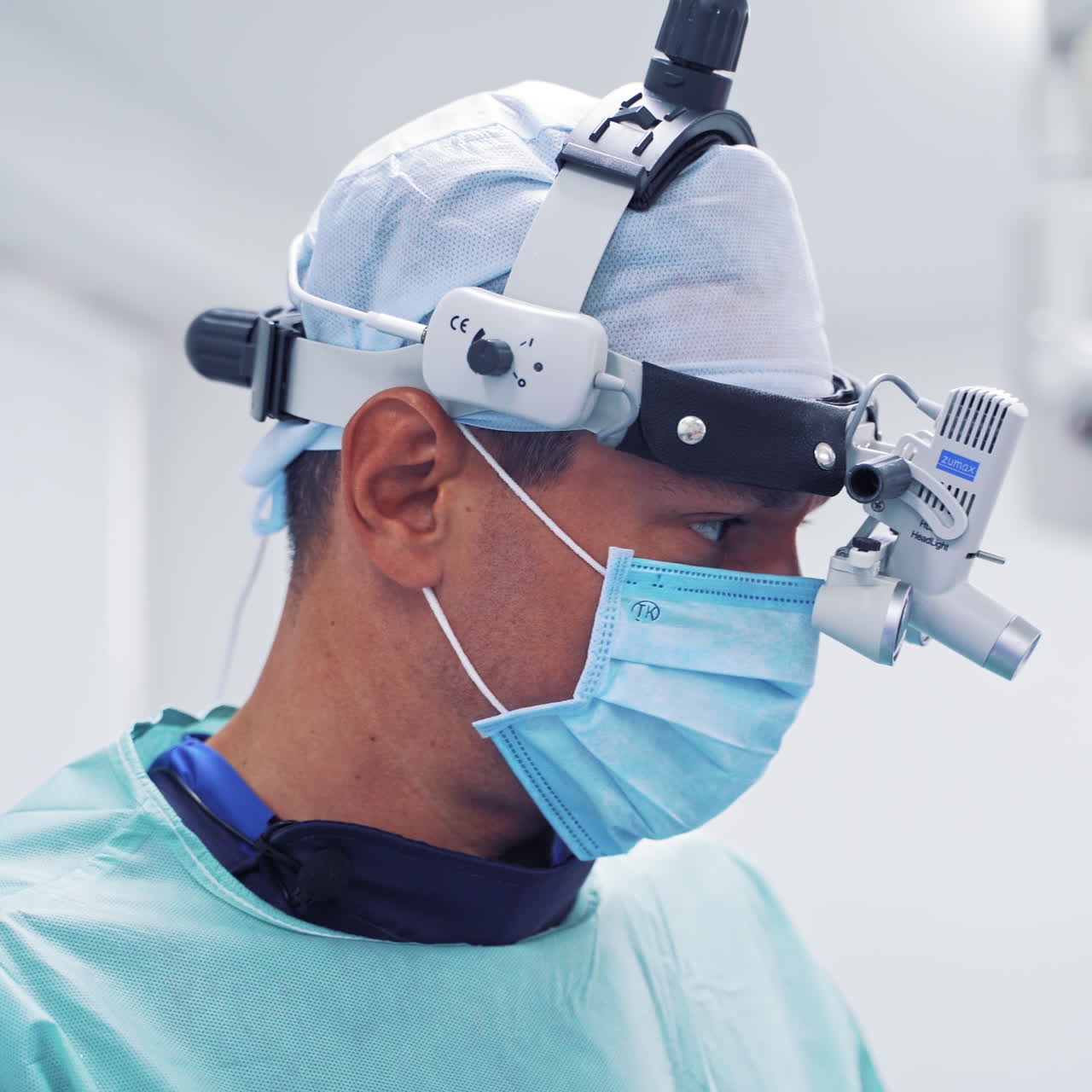 Portrait of a male doctor in a medical mask and protective uniform. Surgeon's face with magnifying glasses in the operating room.