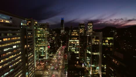 Luftdrohne-über-Santiago,-Chile,-Las-Condes-Avenue-Bei-Nacht,-Wolkenkratzerstraßen,-Hohe-Hochhäuser,-Skyline-Bei-Sonnenuntergang-In-Der-Lateinamerikanischen-Metropole