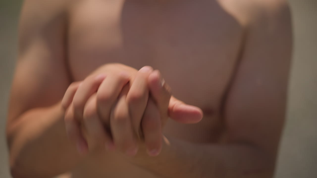 Hombre iluminado por el sol entrelazando los dedos en el exterior; la cálida luz del sol resalta la interacción táctil de los dedos al aire libre; serena escena exterior que muestra a un hombre uniendo los dedos junto a una valla en medio de la cálida luz del sol y la vegetación