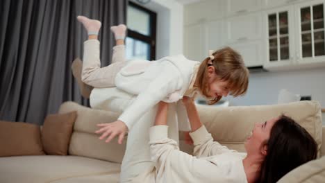 Madre-Alegre-Cargando-A-Una-Niña-Pequeña-De-Rodillas-Fingiendo-Volar-Divirtiéndose-Juntos