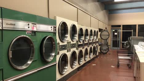 4k uhd handheld footage of a clean, brightly lit, empty laundromat shot from outside at night