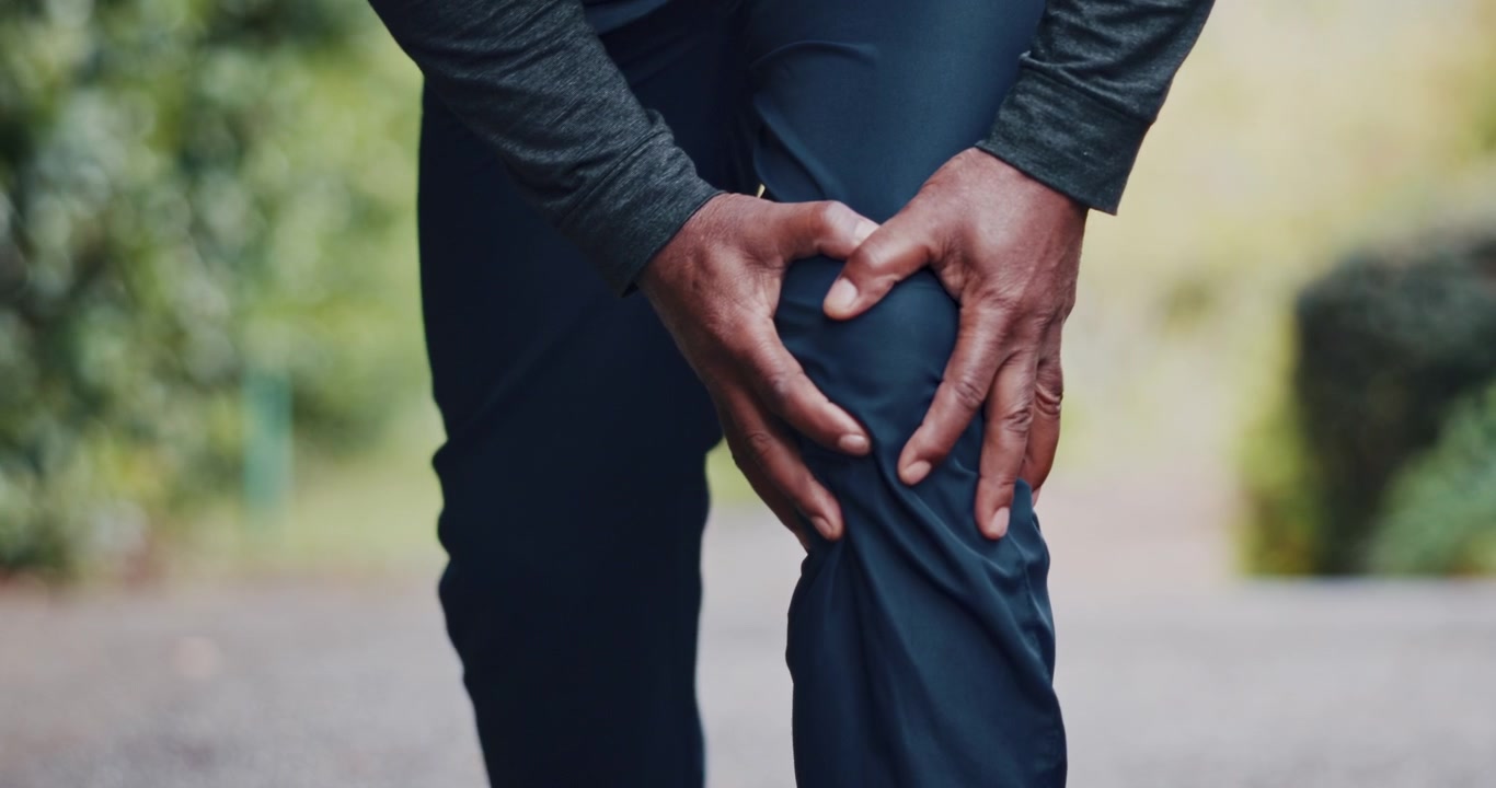 Person Holding Knee in Pain While Standing Outdoors