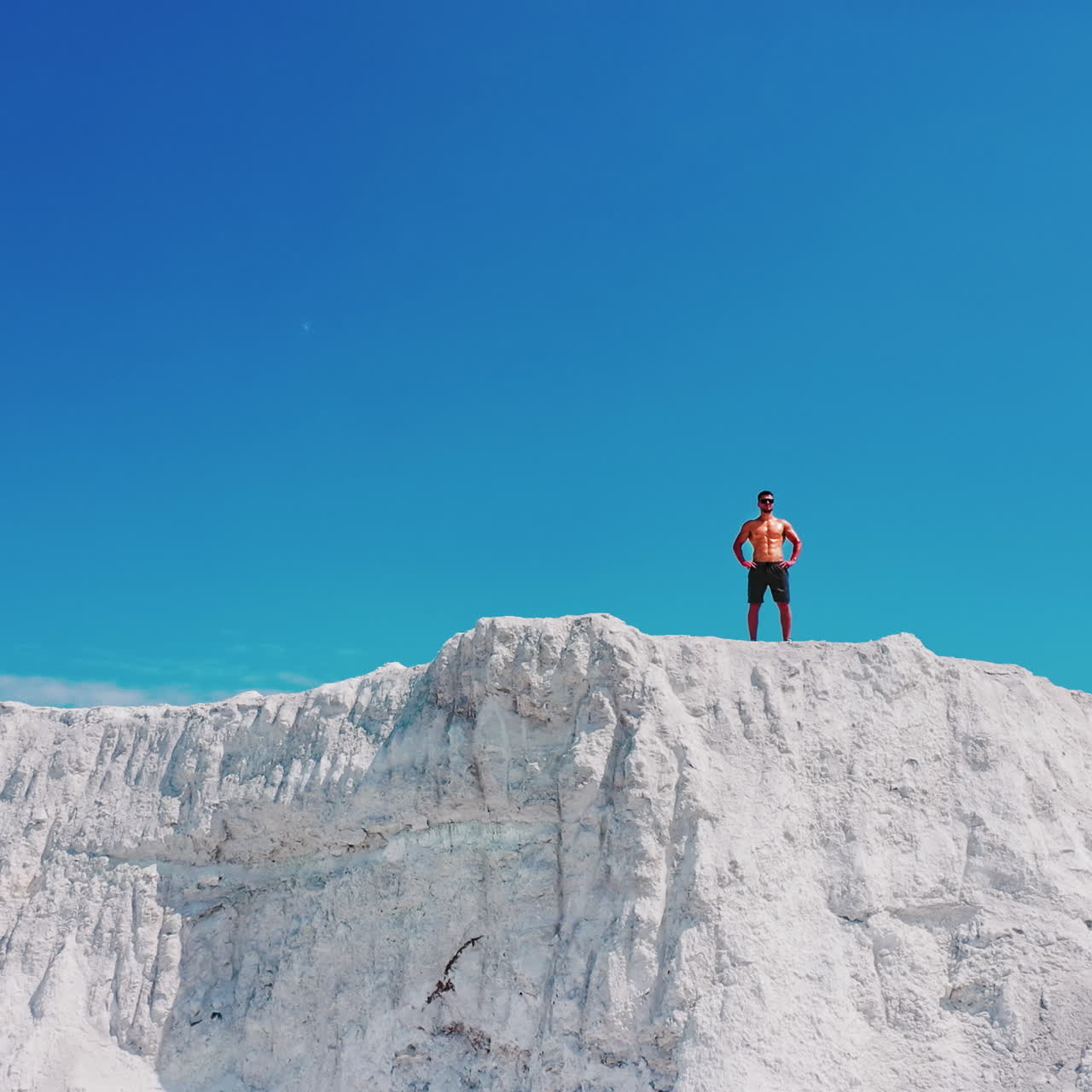 Drone view on a sportive man standing on the edge of the mountain. Shirtless athlete on the top of white canyon under clear sky in summer day.