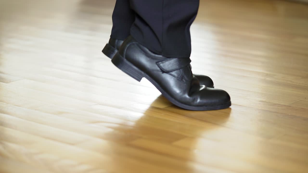Man's legs shows black shoes standing on heels and on socks in turn on the wooden floor. Legs of a teenager in black trousers and the dancing shoes. Close-up