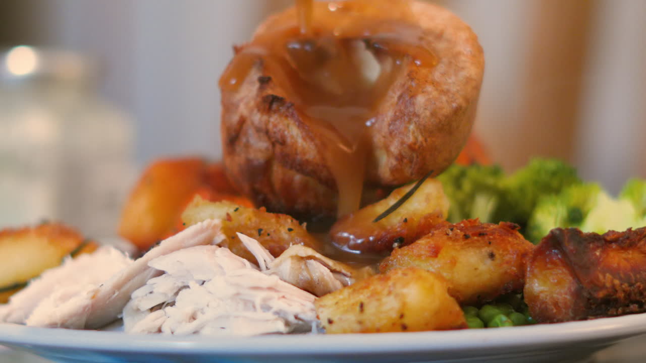 Versamento di salsa (gravy) al rallentatore su un soffice e cavo Yorkshire pudding, con un pranzo arrosto che include pollo, patate e verdure. Ideale per tutorial di cucina, montaggi di comfort food e pubblicità sui social media per ristoranti.