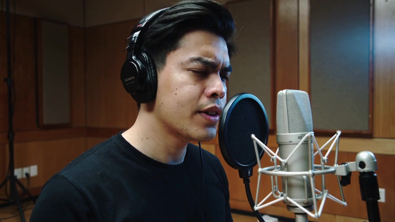 Vocalist asiatico che inspira e canta, registrando in studio con cuffie, maglietta nera e microfono a condensatore.