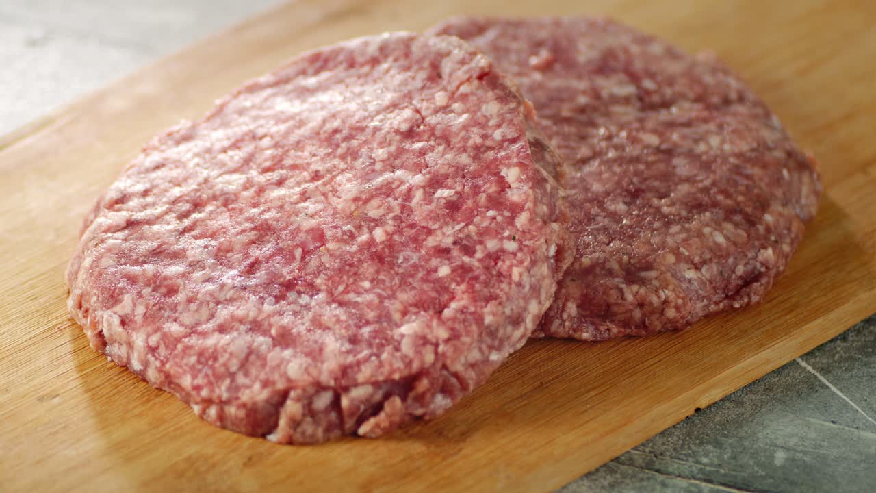 la carne cruda de la hamburguesa gira lentamente en una tabla de madera.