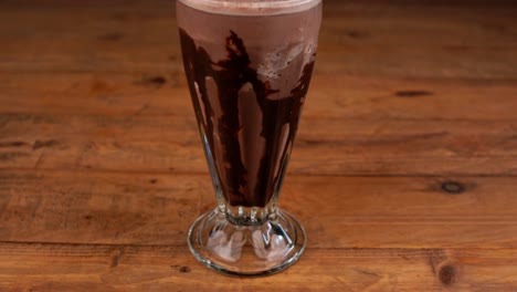 Detailed-close-up-of-chocolate-milkshake,-with-caramel,-espresso-coffee-and-whipped-cream-with-cherry,-tilt-up-and-down