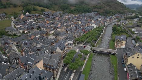 Die-Drohne-Steigt-Anmutig-Zu-Einem-Ruhigen-Flussbett-In-Einer-Malerischen-Spanischen-Stadt-Inmitten-Der-Atemberaubenden-Pyrenäen-Hinab