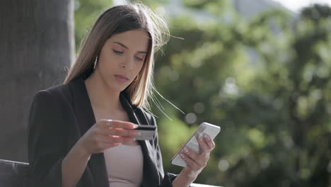 chica con tarjeta de crédito y usando un teléfono inteligente al aire libre