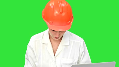 arquitecta pensativa que usa una computadora portátil y un plan de papel para comprobar el progreso en una pantalla verde, llave de croma