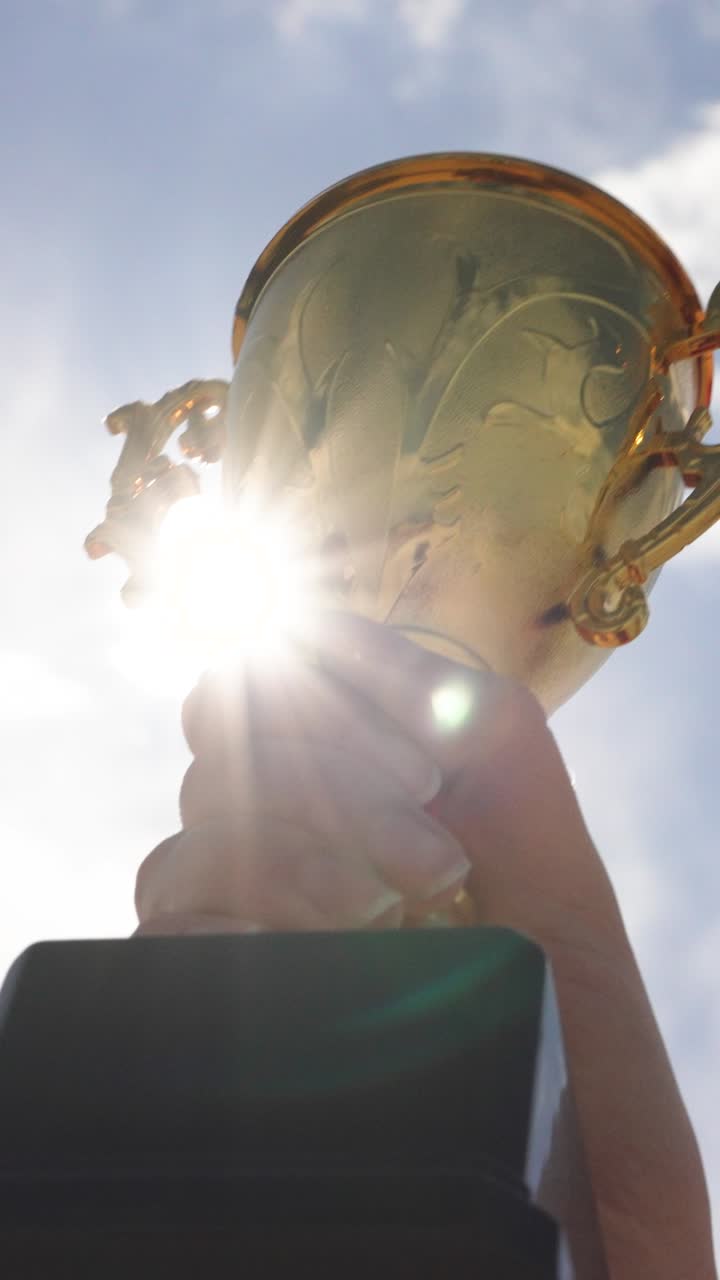 Primo piano di una mano che tiene un trofeo contro lo sfondo del cielo all'aperto. Concetto di realizzazione, successo, vittoria, motivazione e realizzazione personale
