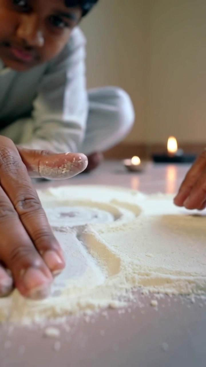 Vertical video: Touching powder, boy in pjs shaping spiral to make floor pattern with ring, candles