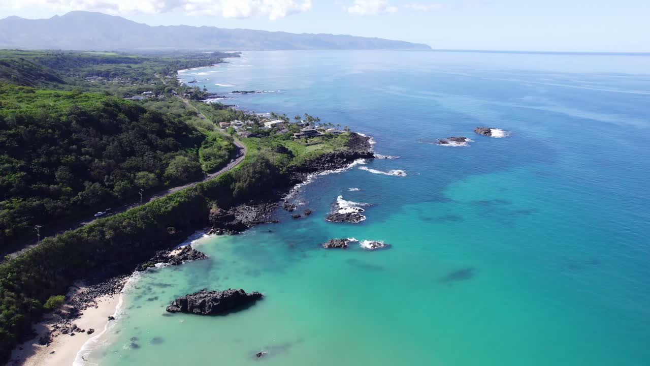 drone footage along the North Shore of Oahu Hawaii with lush vegetation white sand beaches and turquoise blue water of the Pacific ocean with mountains along the horizon