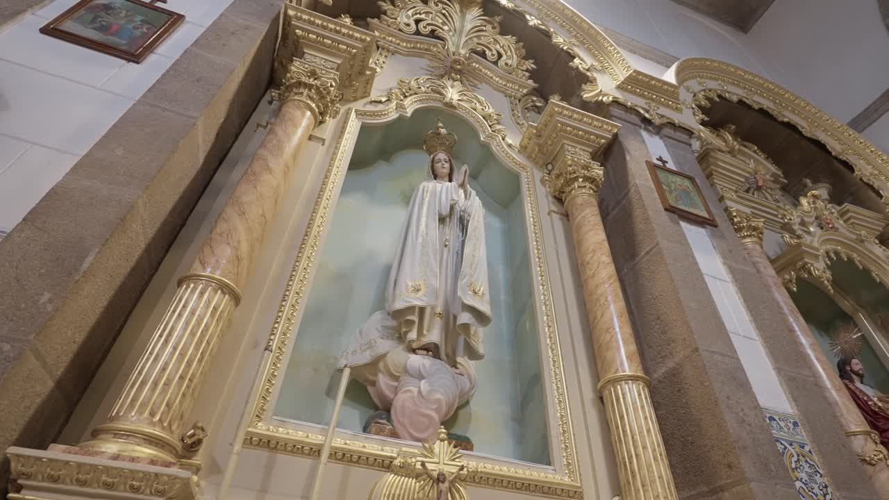 Primo piano della statua della Vergine Maria inquadrata dall'altare dorato all'interno della chiesa