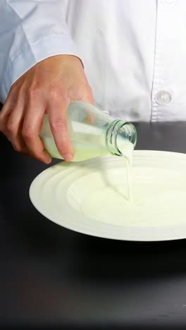 una persona con una bata de laboratorio vierte leche en un plato, rodeado de líquidos de colores, en un entorno controlado
