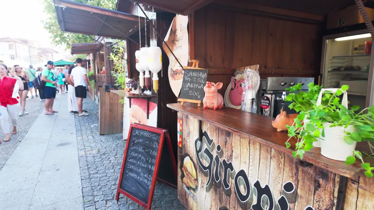 People stroll through outdoor food stalls in Vila Nova de Gaia on a sunny day